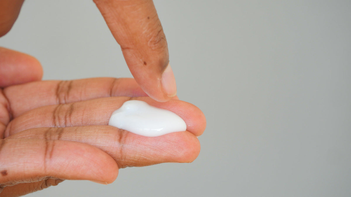 Close-up of fingertips touching a small amount of white cream.